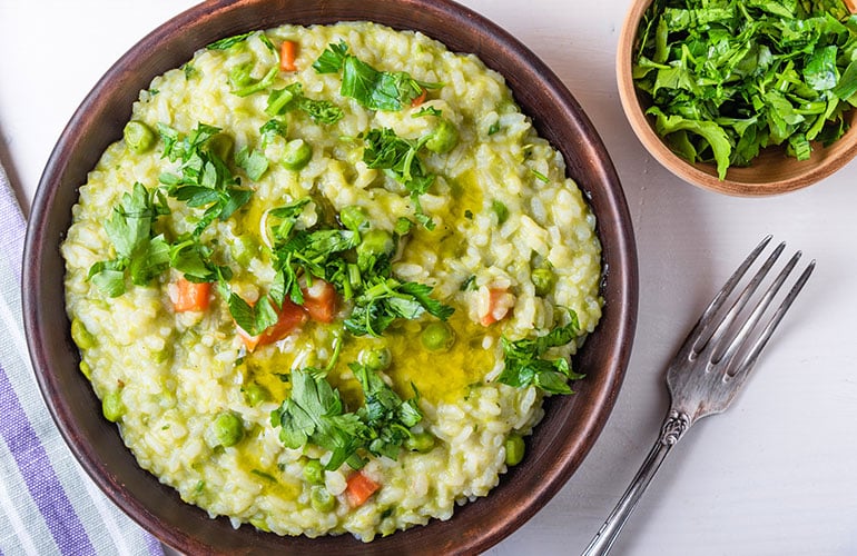 Traditional Italian vegetarian risotto with peas, carrots and parsley in rustic style, closeup